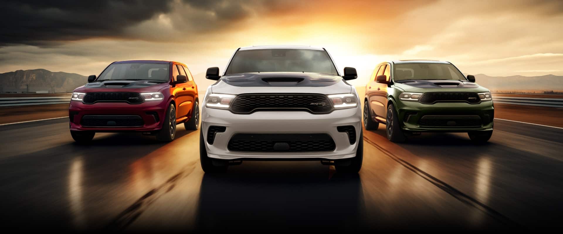 Three 2026 Dodge Durango models being driven on a track at sunset. From left to right: a red Dodge Durango SRT Hellcat, a white Dodge Durango SRT Hellcat and a green Dodge Durango SRT Hellcat.