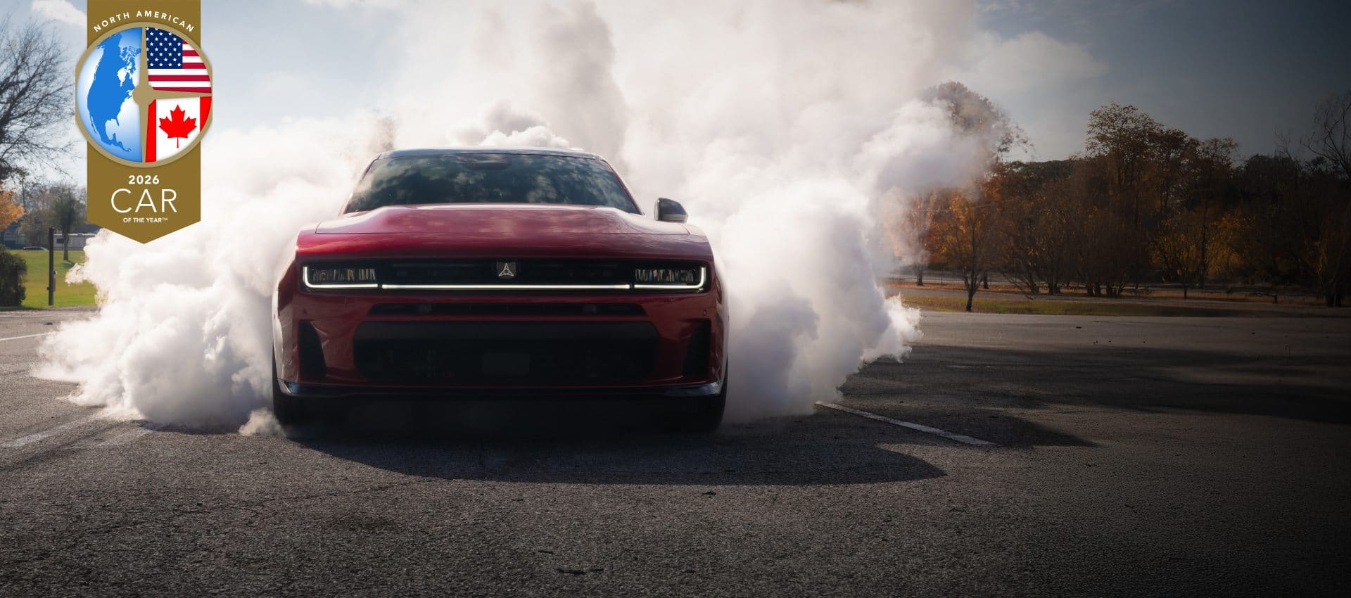 A front end angle of a 2026 Dodge Charger Scat Pack on asphalt, with white smoke billowing from the rear of the vehicle. North American 2026 Car of the Year.