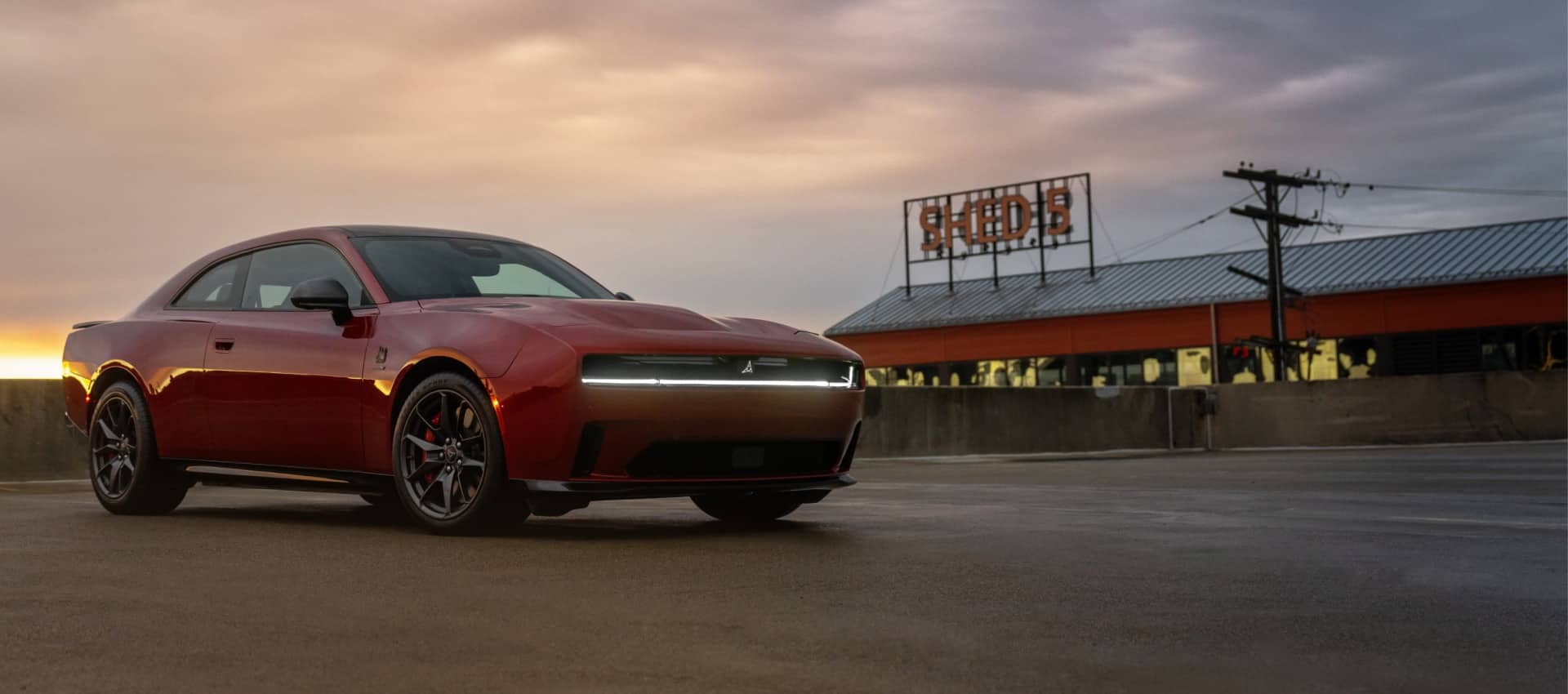 A passenger-side front angle of a red 2025 Dodge Charger Daytona Scat Pack at dusk. Presidents' Day Sales Event.
